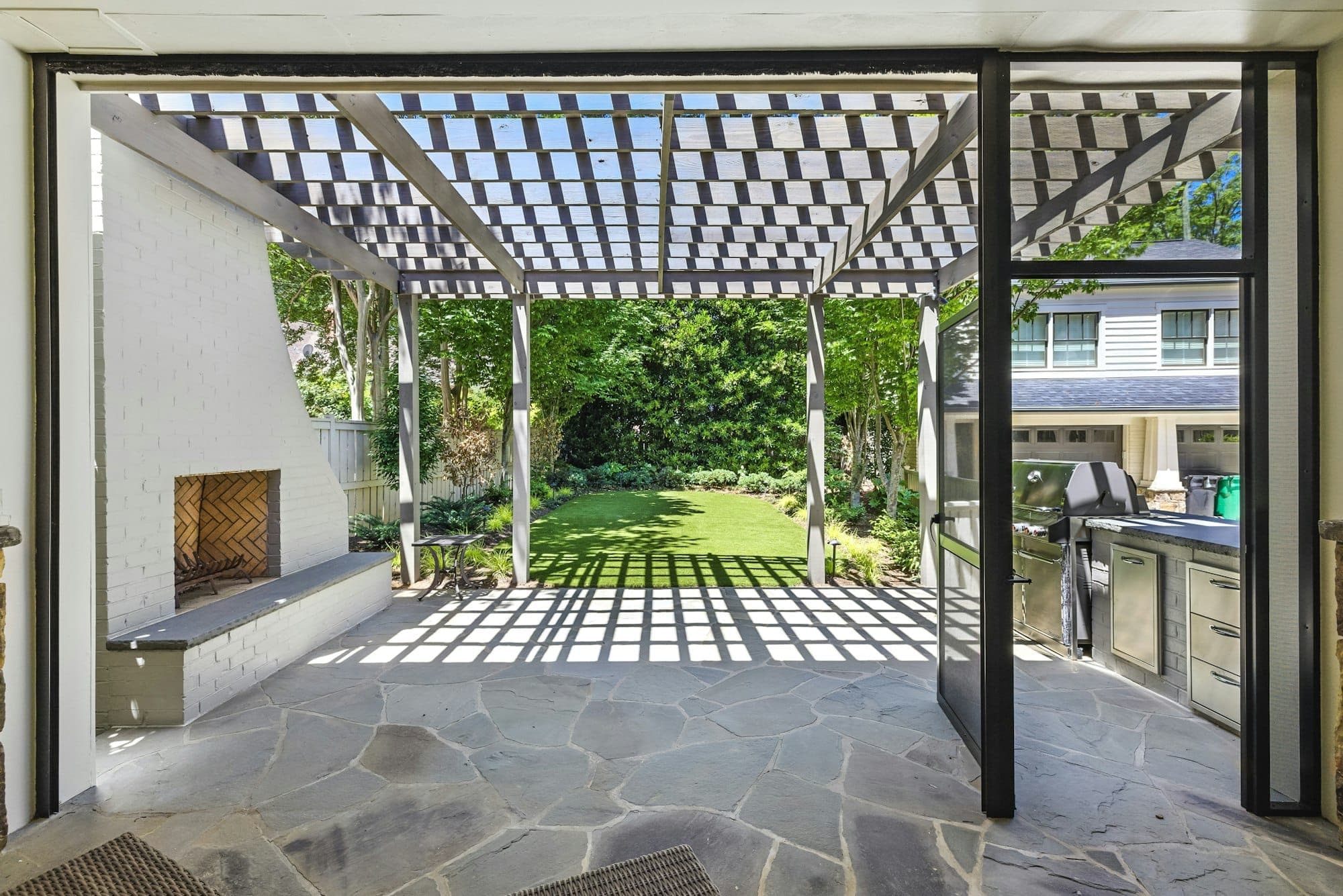 Wood pergola over a flagstone patio with an outdoor fireplace and kitchen